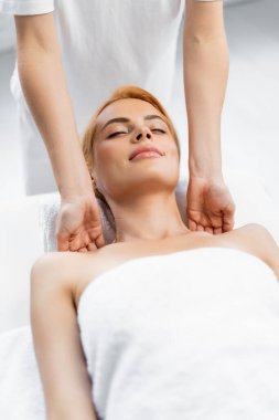 Kapalı gözlü memnun müşteri spa merkezinde omuz masajı yaptırıyor. 