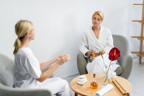 Blonde Client Bathrobe Holding Cup Tea While Looking Blurred Spa — Stock Photo, Image