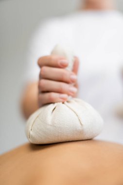Müşteriye masaj yaparken elinde bitki torbası olan masör görüntüsü. 