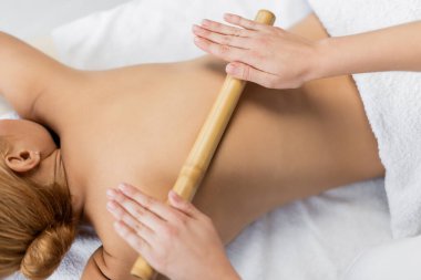 Profesyonel masörün bambu çubuğuyla müşterinin sırtına masaj yapmasının üst görünümü