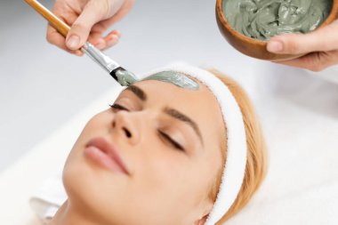 Güzellik uzmanı kaplıcadaki kadının yüzüne kilden maske takıyor.