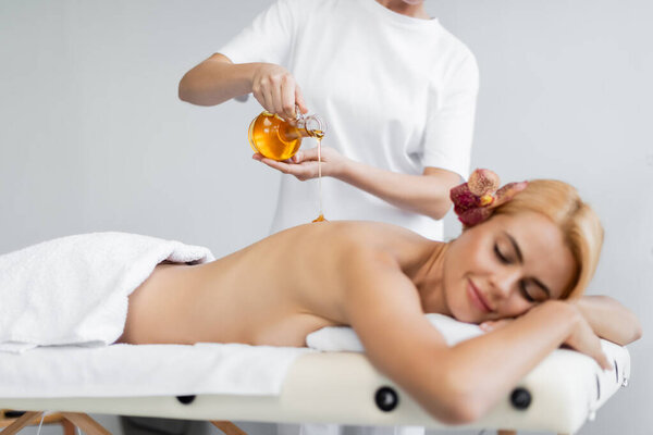 массажист, держащий кувшин, наливая массажное масло на довольного клиента