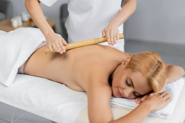 Professioneller Masseur Massiert Rücken Einer Verschwommenen Blonden Kundin Mit Bambusstab — Stockfoto