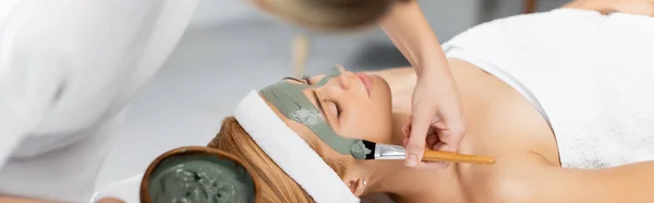美容师拿着碗 在温泉中心的妇女脸上涂上粘土面罩 挂一面横幅 — 图库照片