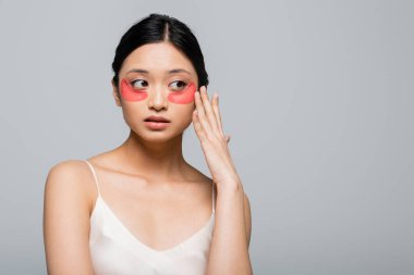 Pretty asian woman touching eye patch on face isolated on grey  clipart