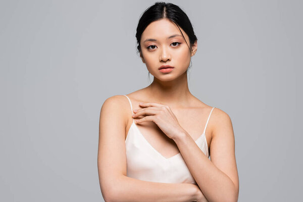 Young asian woman with perfect skin looking at camera isolated on grey 