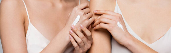 Обрезанный вид женщин в атласных платьях и кремах на руках, изолированных на сером, баннер 