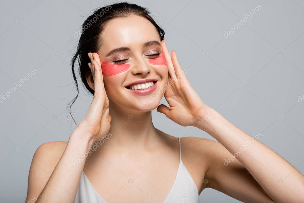 Smiling woman with eye patches touching face isolated on grey