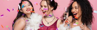 Neşeli çok kültürlü kadınlar pembe arka planda konfeti altında şampanya tutuyorlar. 