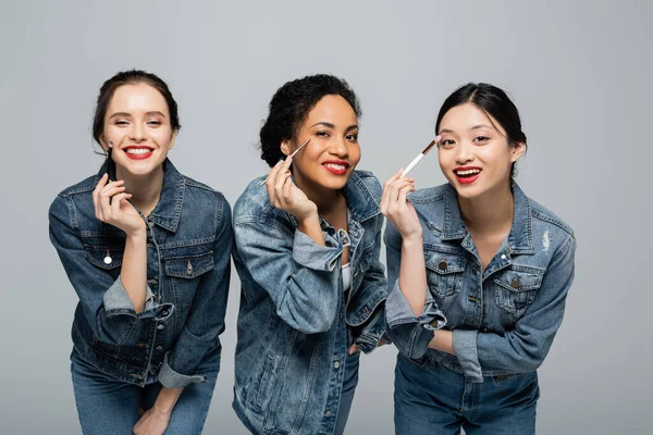 Usmívající Multietnické Ženy Džínových Bundách Držící Kosmetické Kartáče Dívající Kameru — Stock fotografie