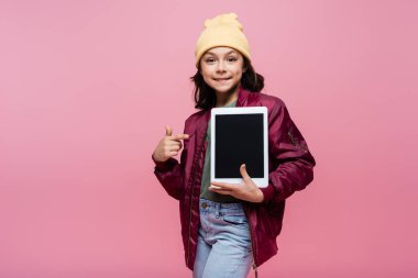 Moda kıyafetli mutlu ergen kız pembe ekranlı boş ekranlı dijital tableti işaret ediyor. 