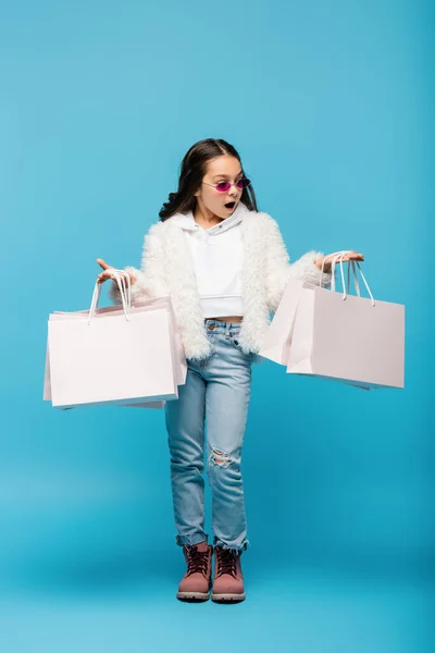ショッピングバッグを持つピンクのサングラスとフェイクファーのジャケットのショッピングバッグの完全な長さ — ストック写真