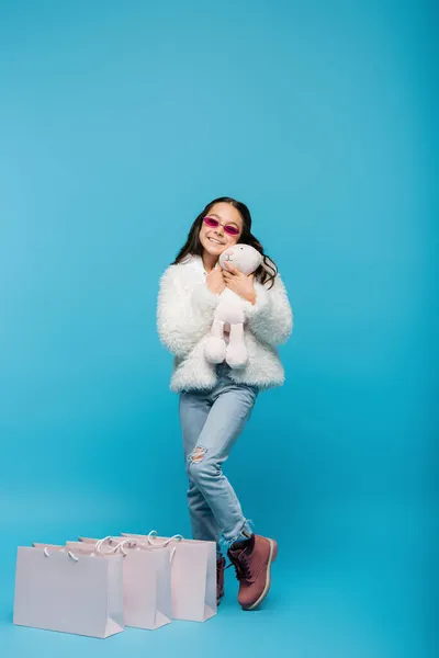분홍색 선글라스를 소녀와 쇼핑백 근처에 부드러운 토끼를 재킷을 소녀의 — 스톡 사진