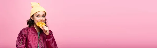 穿着冬装的时髦少女咬着粉色横幅上的棒棒糖 — 图库照片
