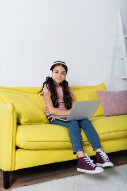 Kablosuz kulaklıklı gülümseyen genç kız evde internetten ders çalışıyor.