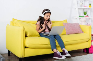 Kablosuz kulaklık takan genç bir kız evde internetten okurken video görüşmesi sırasında konuşuyor.