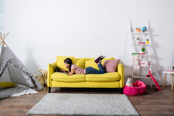 preteen child lying on sofa and using laptop in modern living room