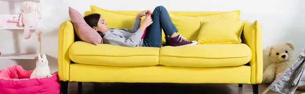 自宅のソファに横になって本を読んでいる少女バナーの側面図 — ストック写真