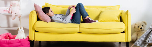 side view of preteen girl reading book while lying on couch at home, banner