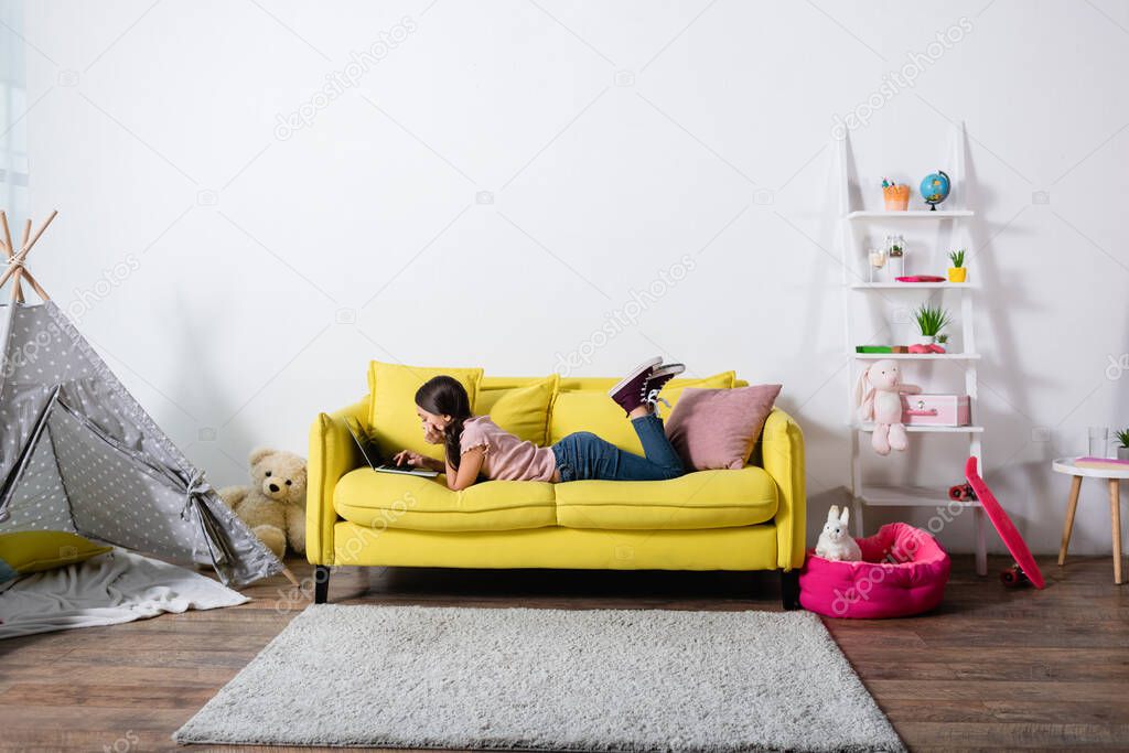 preteen child lying on sofa and using laptop in modern living room