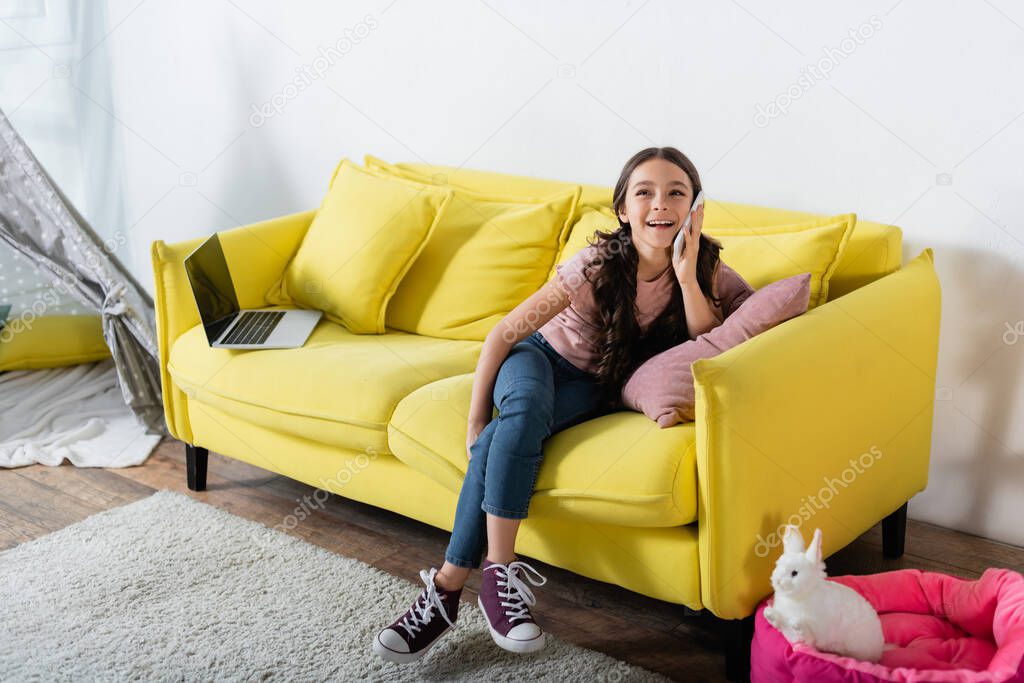 preteen girl smiling while talking on smartphone in living room 