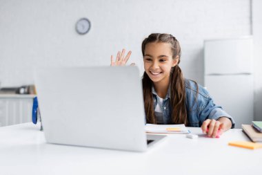 Mutfaktaki bulanık laptopta video görüşmesi yapan gülümseyen kız. 