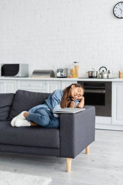 Çocuk mutfaktaki kanepede dizüstü bilgisayarın yanında oturuyor. 
