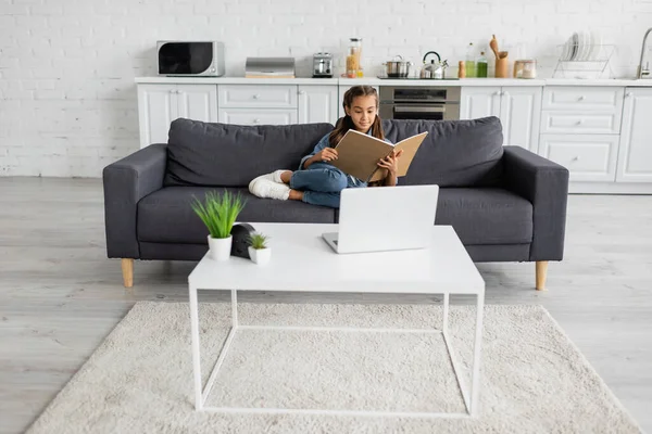 Preteen Kind Hält Notizbuch Auf Couch Neben Laptop Auf Couchtisch — Stockfoto