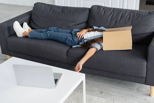 Mädchen Mit Notizbuch Gesicht Liegt Auf Couch Neben Verschwommenem Laptop — Stockfoto