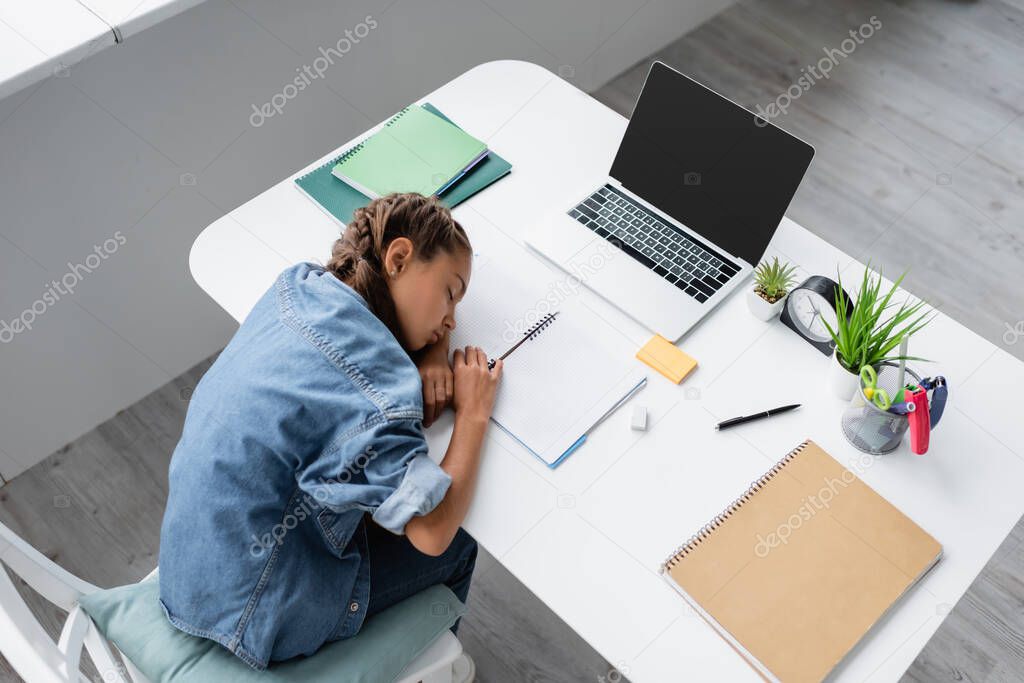 Top view of preteen child sleeping near laptop and notebooks on table at home 