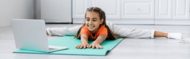 Gülümseyen çocuk dizüstü bilgisayarın yanında spor minderinin üstünde, pankartta 