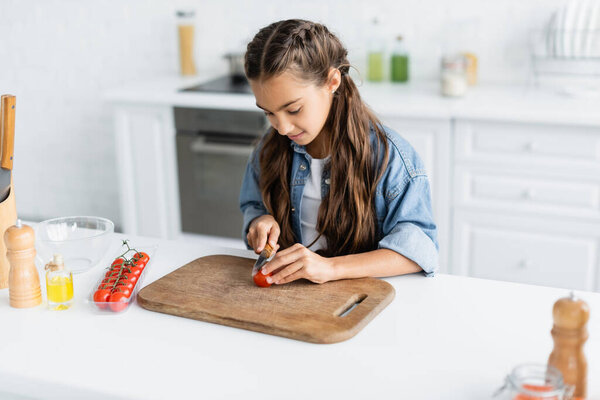 Kid cutting cherry tomato near olive oil in kitchen 