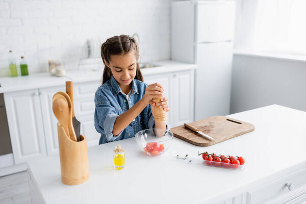 Smiling girl seasoning cherry tomatoes in bowl in kitchen 