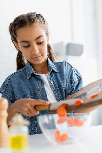 Kid pouring cherry tomatoes in blurred bowl in kitchen 