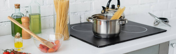 Macaroni in saucepan on stove near cherry tomatoes in kitchen, banner 