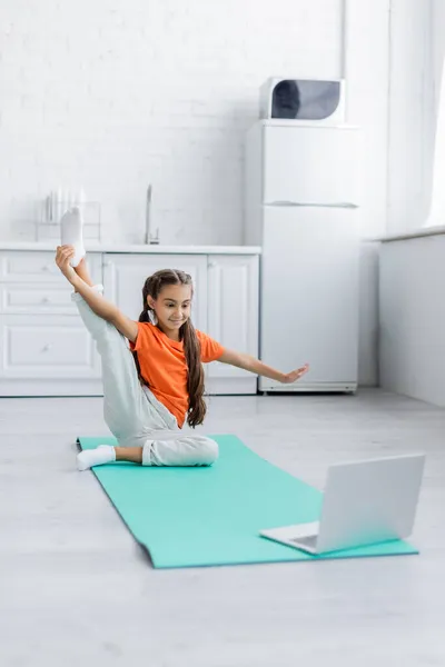 Criança Sorridente Esticando Tapete Fitness Perto Laptop Casa — Fotografia de Stock
