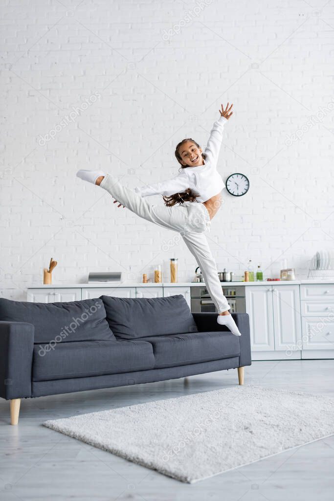 Happy preteen child jumping near couch in kitchen 