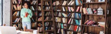 Genç Afro-Amerikalı gözlüklü öğrenci, elinde tahta merdiven ve masasında cihazlar bulunan bir kitap tutuyor.