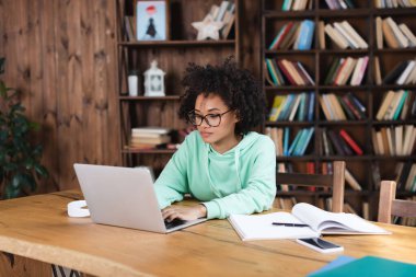 Gözlüklü Afro-Amerikan öğrenci akıllı telefon ve kulaklık yanında dizüstü bilgisayar kullanıyor.