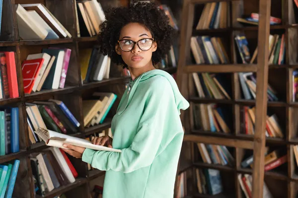 Jong Afrikaans Amerikaans Student Bril Holding Boek Buurt Van Boekenkast — Stockfoto