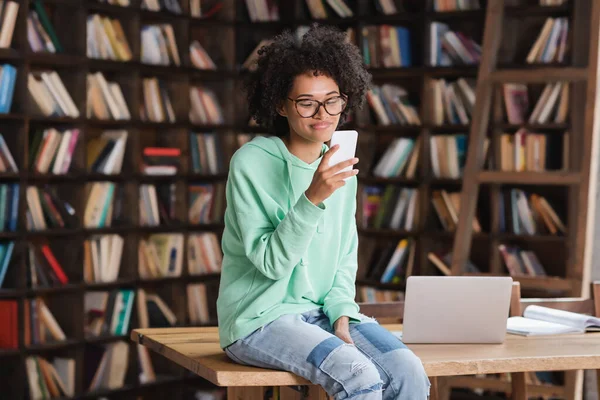 Cheerful African American Student Eyeglasses Holding Smartphone Sitting Desk Laptop — Stock Photo, Image