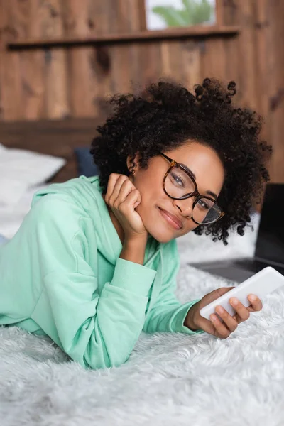 Lächelnde Afroamerikanerin Mit Brille Auf Dem Bett Liegend Und Smartphone — Stockfoto