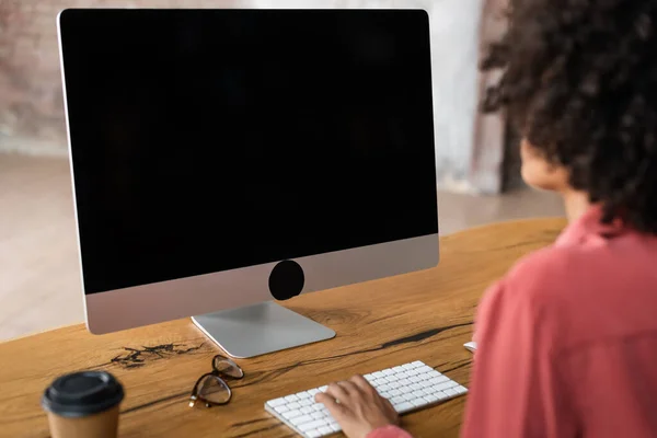 アフリカ系アメリカ人の女性がコンピュータのキーボードを使って机の上のぼやけた紙コップや眼鏡の近くで — ストック写真