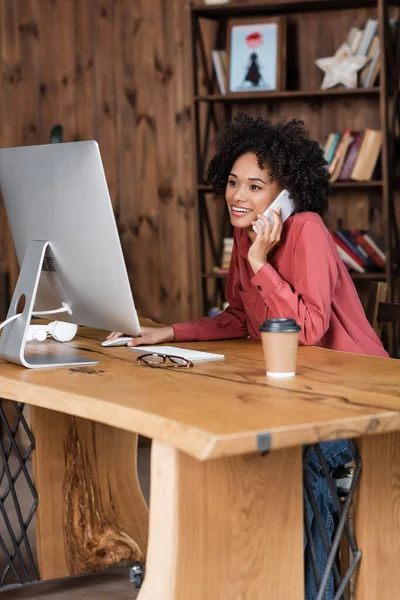 Alegre Mujer Afroamericana Hablando Teléfono Inteligente Cerca Monitor Taza Papel — Foto de Stock