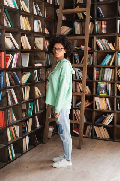 Young African American Student Eyeglasses Standing Bookcase Ladder — Stock Photo, Image