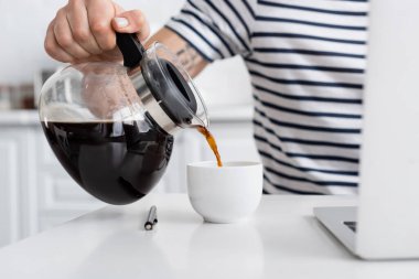 Evdeki bulanık dizüstü bilgisayarın yanına kahve döken adam görüntüsü. 