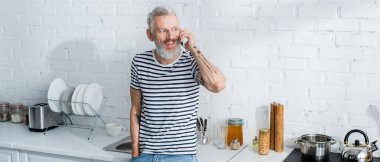 Smiling man talking on smartphone in kitchen, banner. Translation: 