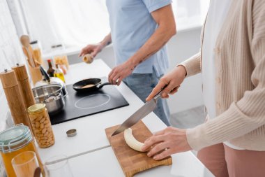 Cropped view of woman cutting banana near blurred husband cooking in kitchen  clipart