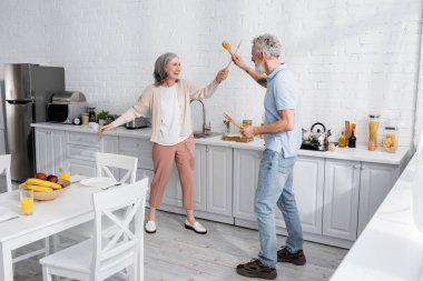 Mutfakta tahta spatulalarla kavga eden mutlu olgun bir kadın. 