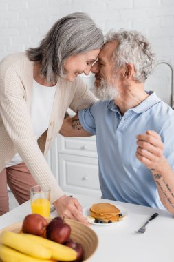 Side view of couple smiling near breakfast in kitchen. Translation: 